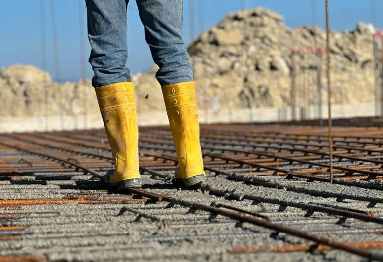 Se muestra imagen de botas de un trabajador sobre obra civil en proceso.